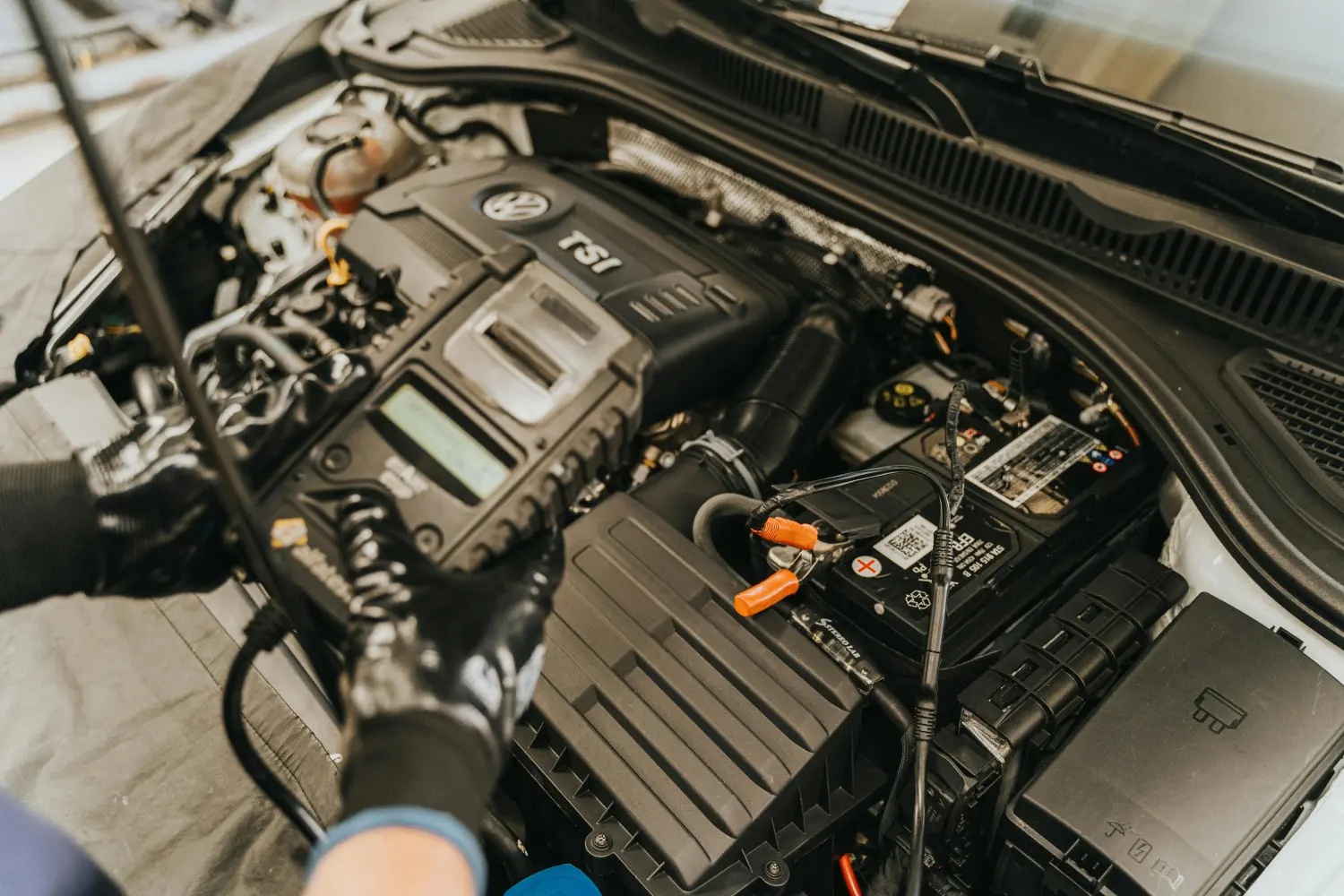 Eine Person, die unter der Motorhaube an einem Automotor arbeitet.